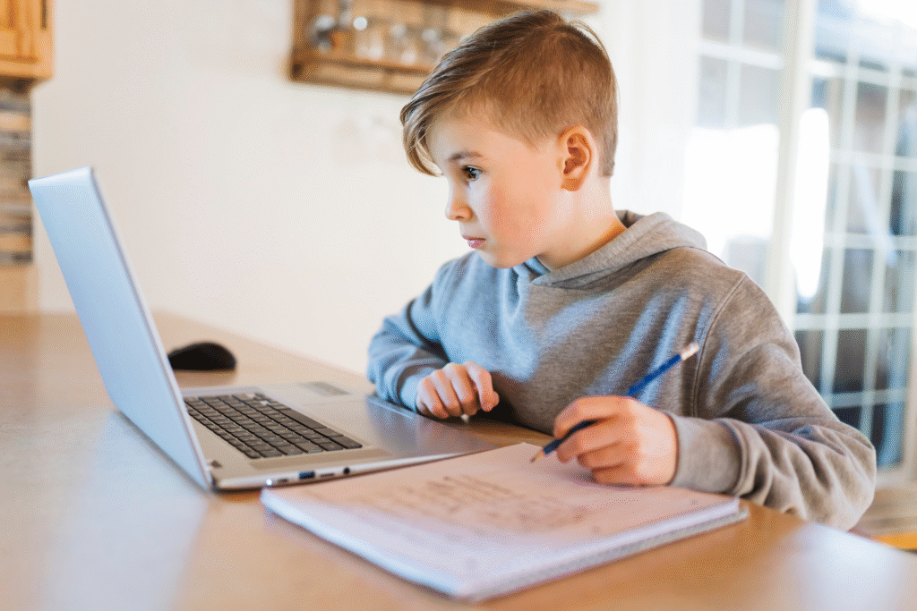 A homeschooling student watches a program on his computer while taking notes